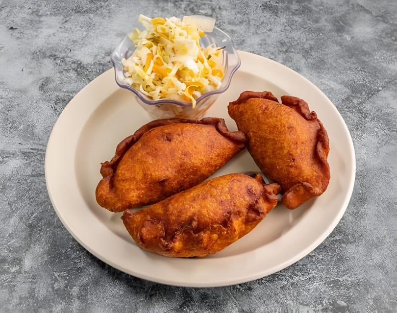 Three golden-brown fried empanadas and a small bowl of coleslaw on a white plate.