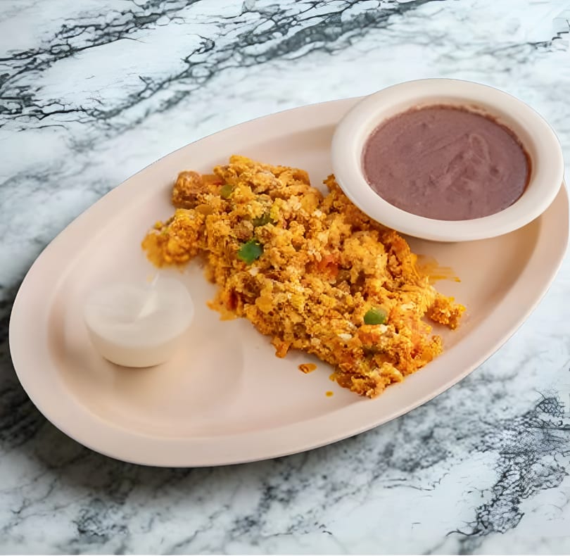 Scrambled eggs with green peppers, a side of refried beans, and sour cream on a marble table.
